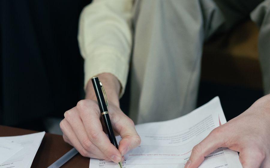 Dos personas firmando documentos sobre una mesa de reuniones.