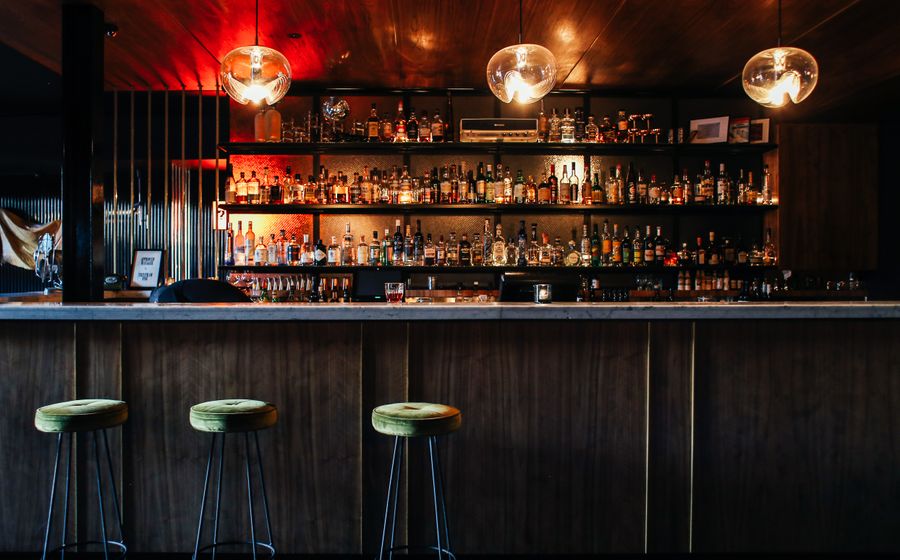 Barra de un bar vacía al cierre, con los taburetes alineados y las botellas al fondo.