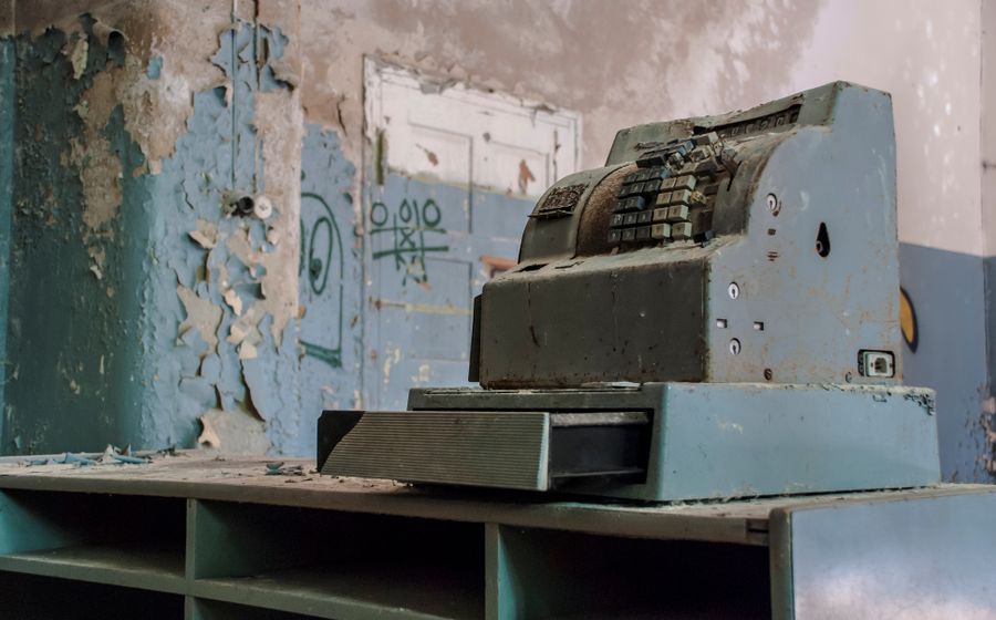 Caja registradora antigua y oxidada en un local abandonado, con el cajón abierto.