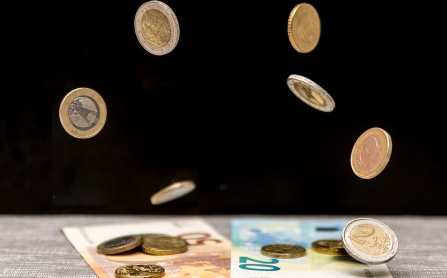 Monedas de euro cayendo sobre unos billetes, con el fondo oscuro.