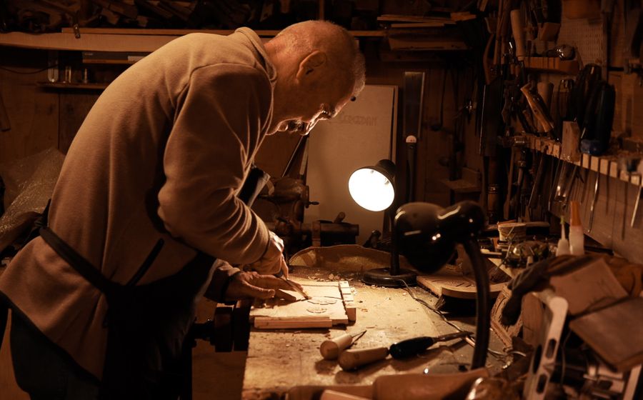 Artesano mayor trabajando la madera en su taller, con las herramientas colgadas detras.