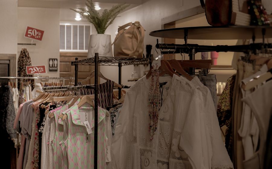 Interior de una tienda de ropa pequeña con las perchas llenas y carteles de rebajas.